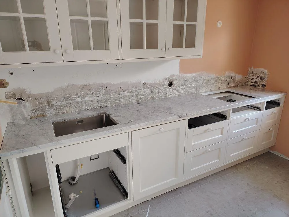 Köksbänkskiva i polerad vit Carrara C-marmor, 30 mm, med lågt stänkskydd, uttag för dubbelho och vita shakerluckor i Bromma.