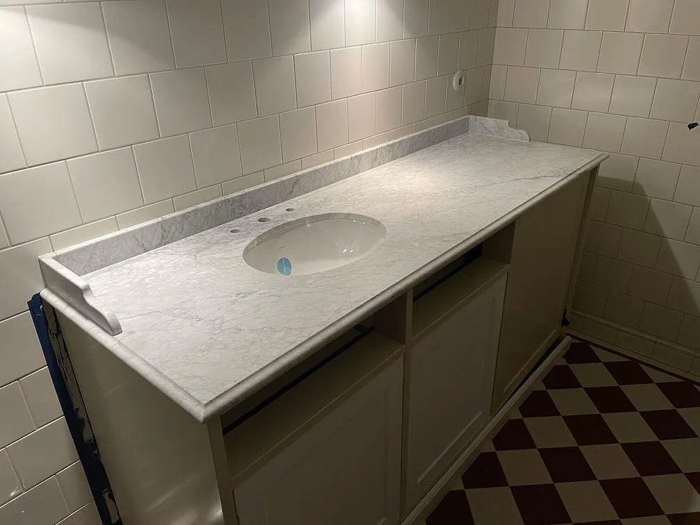 Kommodskiva i vit Carrara C-marmor, matt yta, med underlimmat ovalt tvattstall och uppvikt stankkant i ett badrum i Bromma.