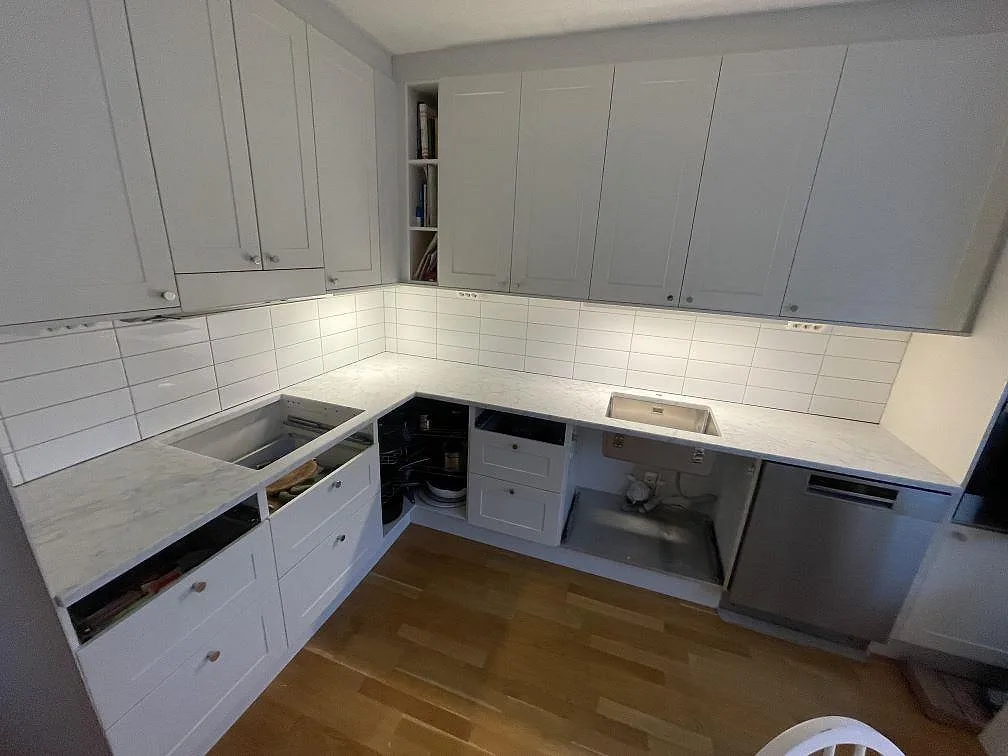 Köksbänkskiva i vit Carrara C marmor, polerad, monterad i U-form i ett kök i Bromma under montering med underlimmad rostfri diskho och urtag för induktionshäll.