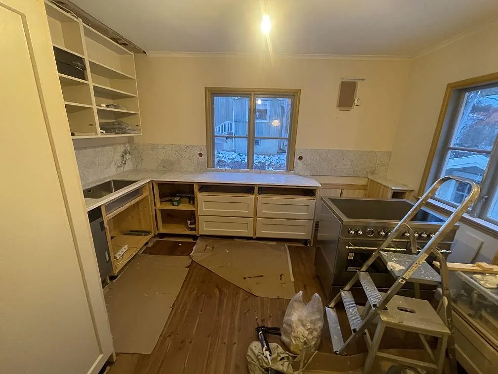 Köksbänkskiva i vit Carrara C-marmor, matt, i ett L-format kök i Bromma med heltäckande marmorstänkskydd och fristående spis under montering.