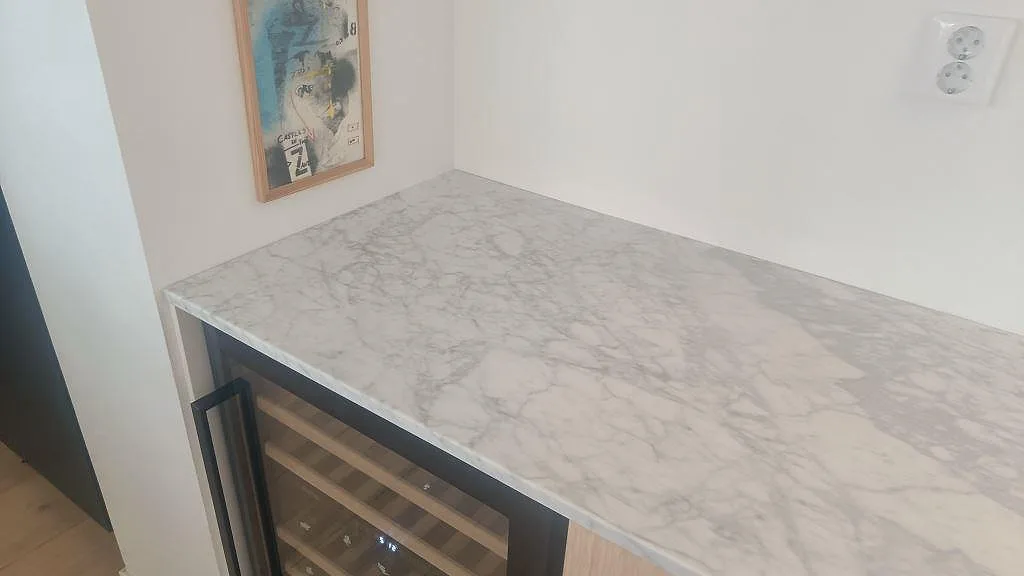 Närbild av polerad Carrara C marmor som bar- och sideboardtopp med grå ådring ovanför vinkyl i Bunkeflostrand.