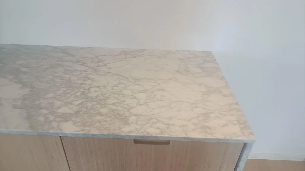 Detalj av 20 mm polerad Carrara C marmor på trätonad sideboardmöbel med ljus ådring i Bunkeflostrand.