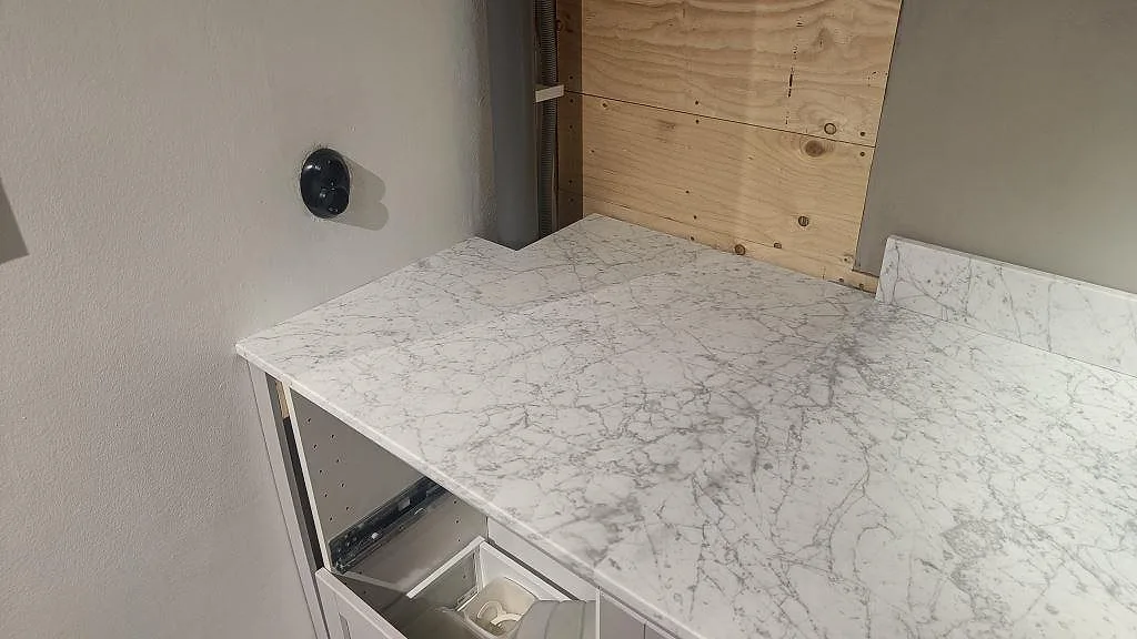 Närbild på matt Carrara C marmorbänkskiva med grå ådring och uppvikt stänkkant vid köksvägg i Bunkeflostrand.