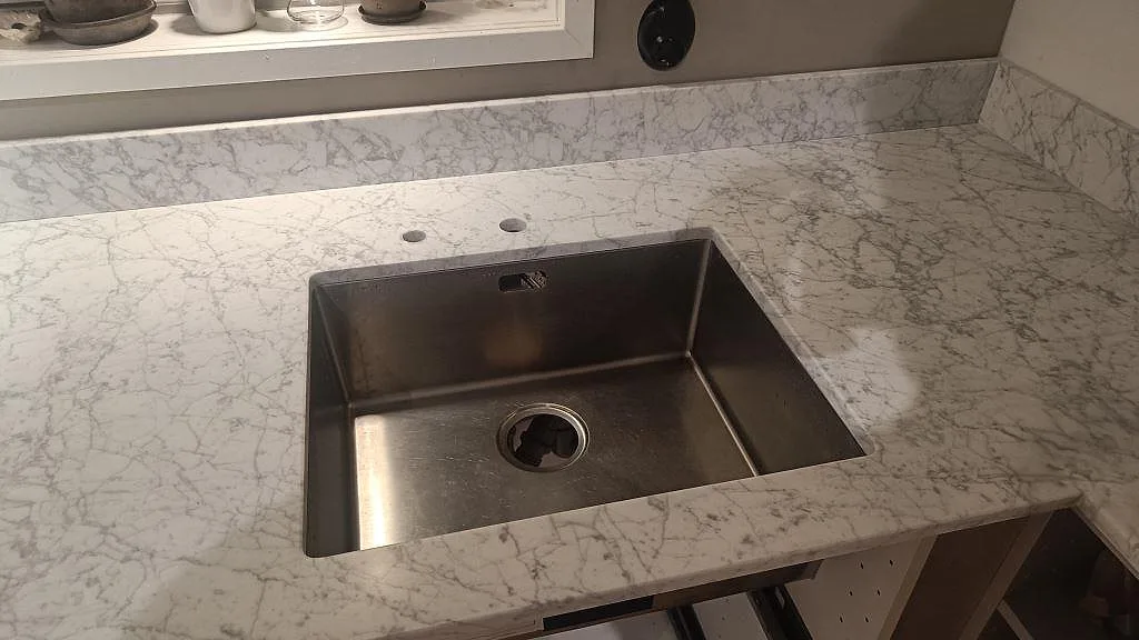 Detalj av köksbänkskiva i matt Carrara C marmor med diskho och grå ådring i Bunkeflostrand.