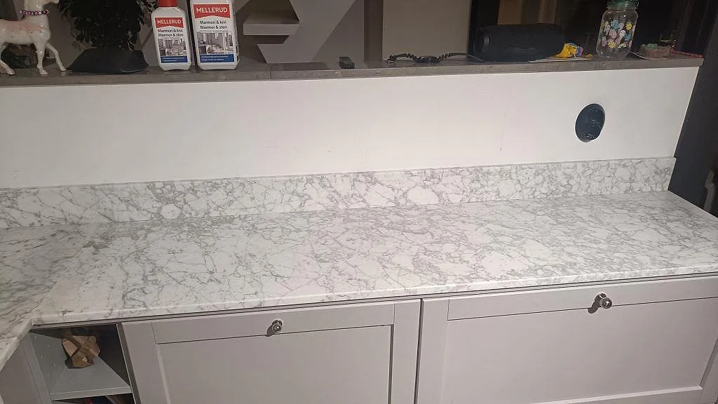 Lång bänkyta i matt Carrara C marmor med låg stänkkant över skåpstommar under montering i Bunkeflostrand.