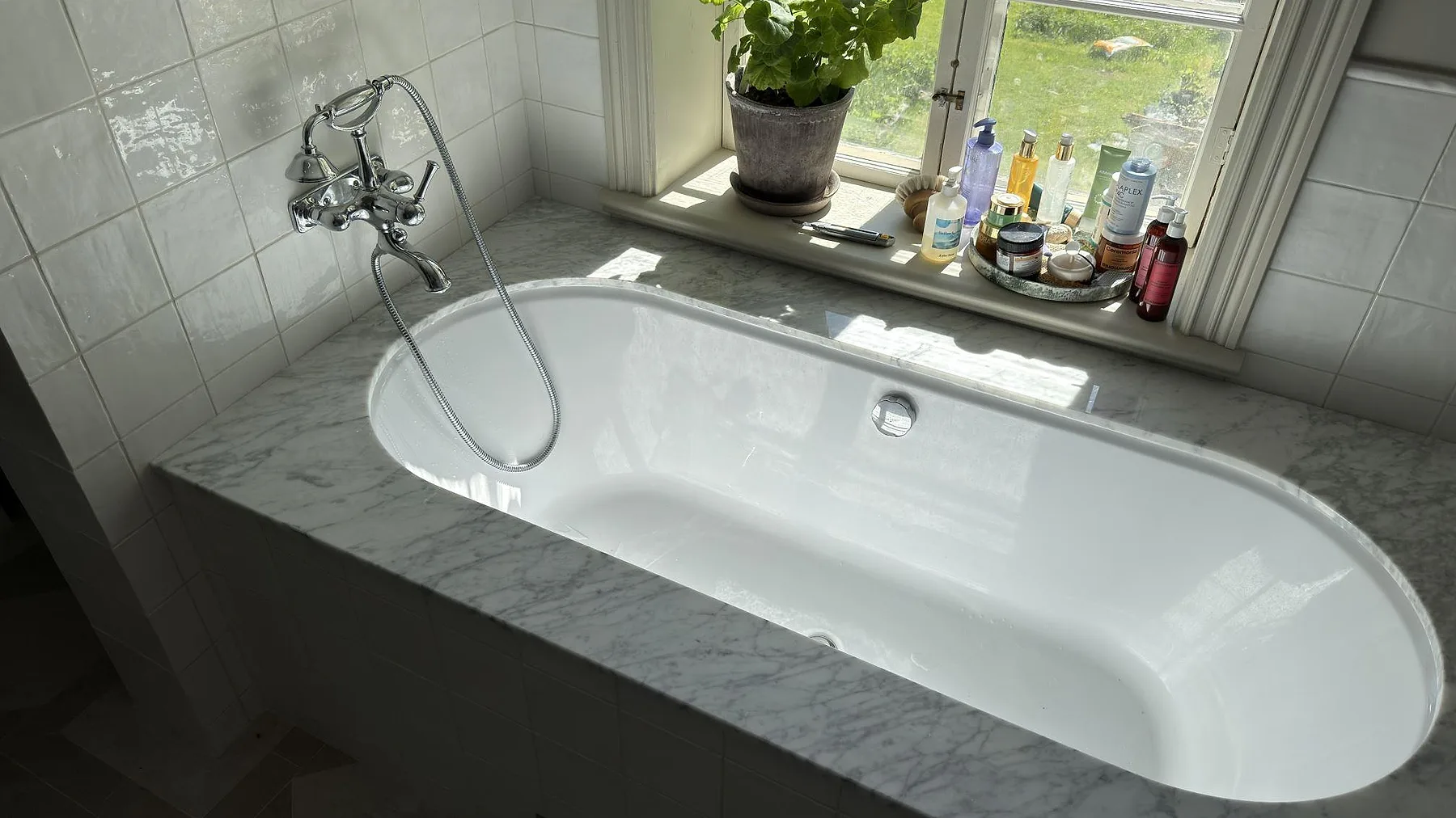 Fristående badkar inramat av polerad Carrara C-marmor i ett ljust badrum i By Kyrkby, med marmorns naturliga ådring i blickfånget.