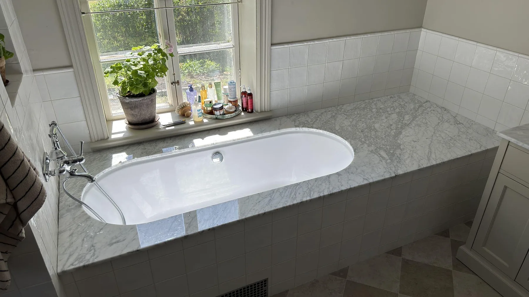 Polerad Carrara C-marmor som badkarssarg vid ett fönster i ett badrum i By Kyrkby, med synlig grå ådring i den vita marmorn.