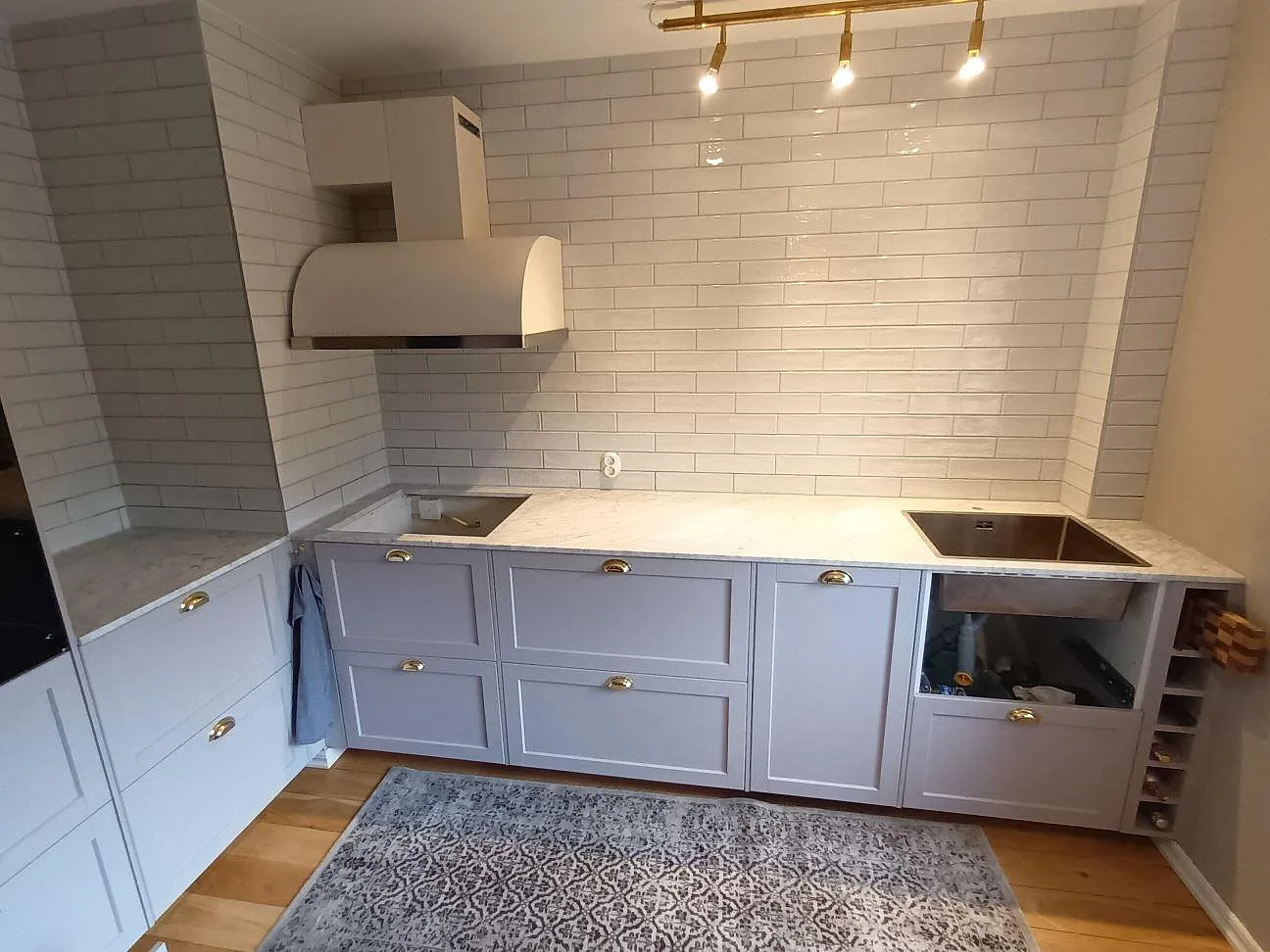 Köksbänkskiva i vit Carrara C marmor med grå ådring, matt yta, med underlimmad rostfri diskho och plats för häll i ett kök med vitt kakel i Danderyd.