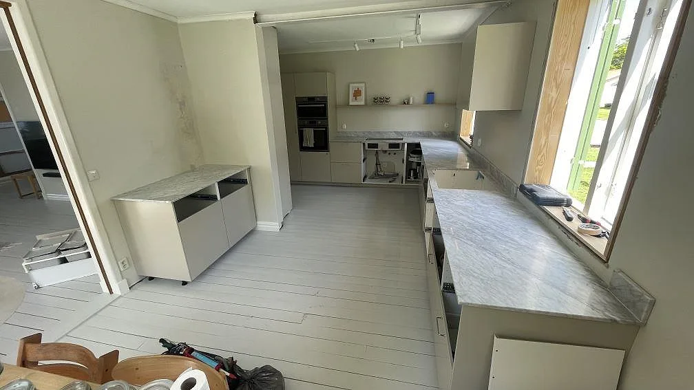 Översikt över kök i Diö med matt köksbänkskiva i Carrara C marmor, uppvikt stänkkant, öppna stommar och fönsterljus.