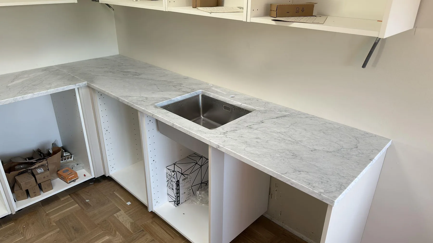 Matt köksbänkskiva i Carrara C marmor med synlig diskho och grå ådring längs väggskåpen i Djursholm.