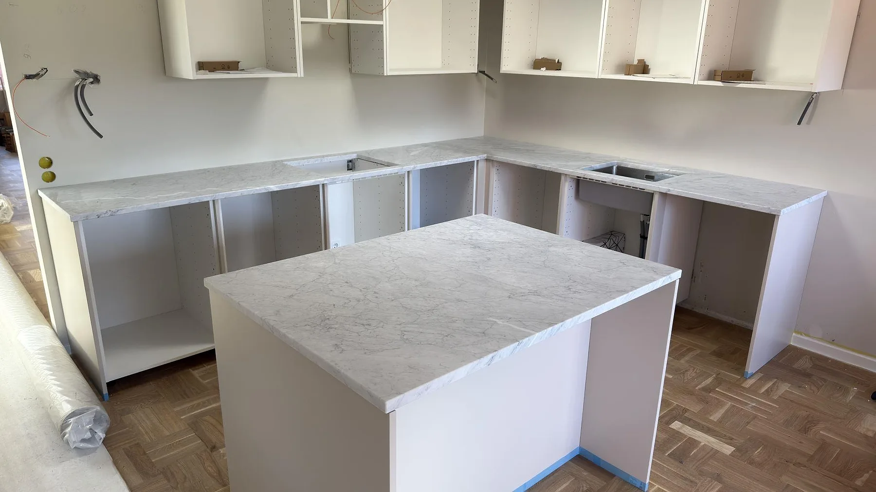 Köksbänkskiva och köksö i matt Carrara C marmor, 30 mm, monterade i ett kök under byggfas i Djursholm.