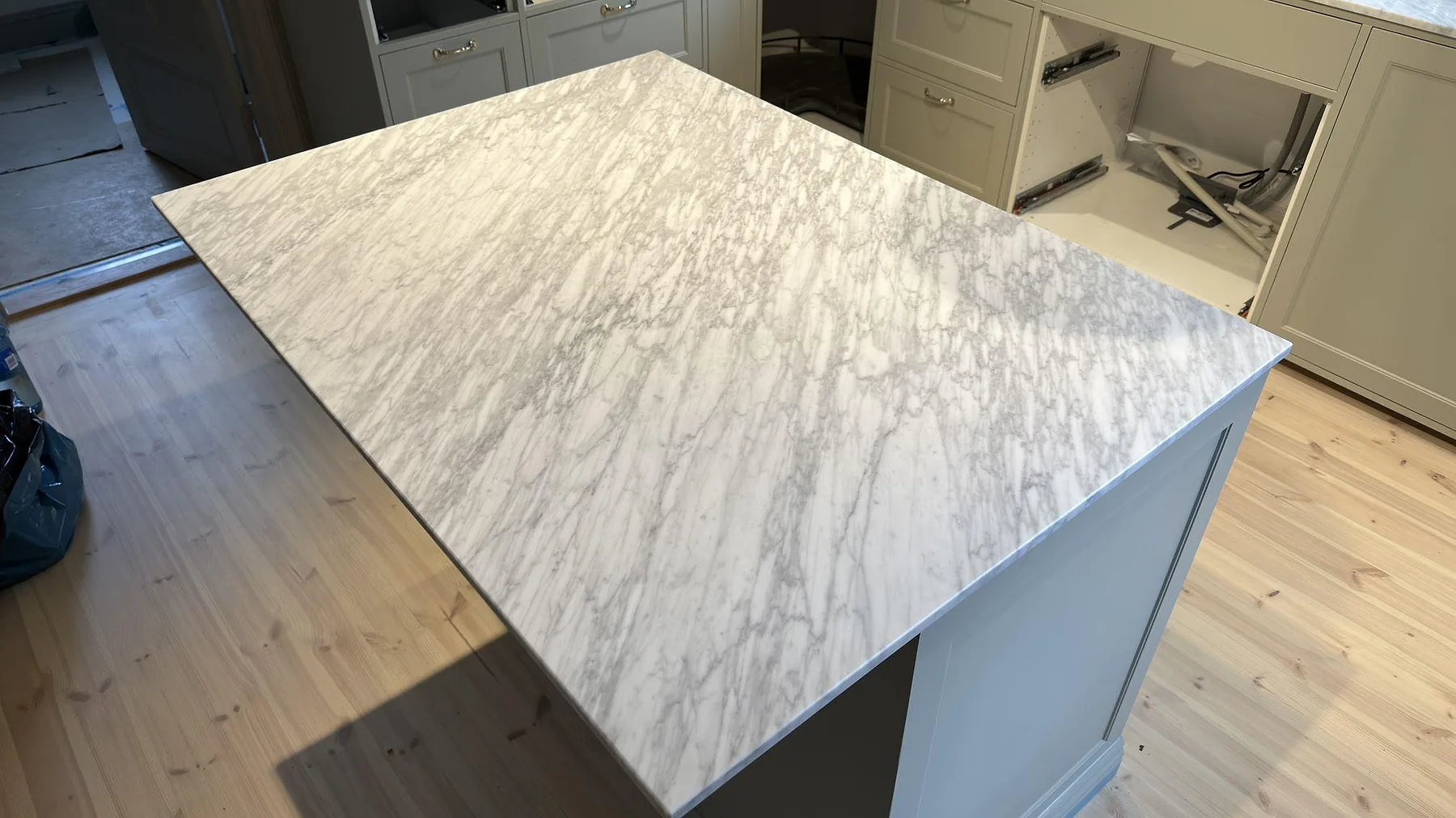 Närbild av matt köksö i Carrara C marmor i Djursholm, där den grå ådringen syns över den stora arbetsytan.