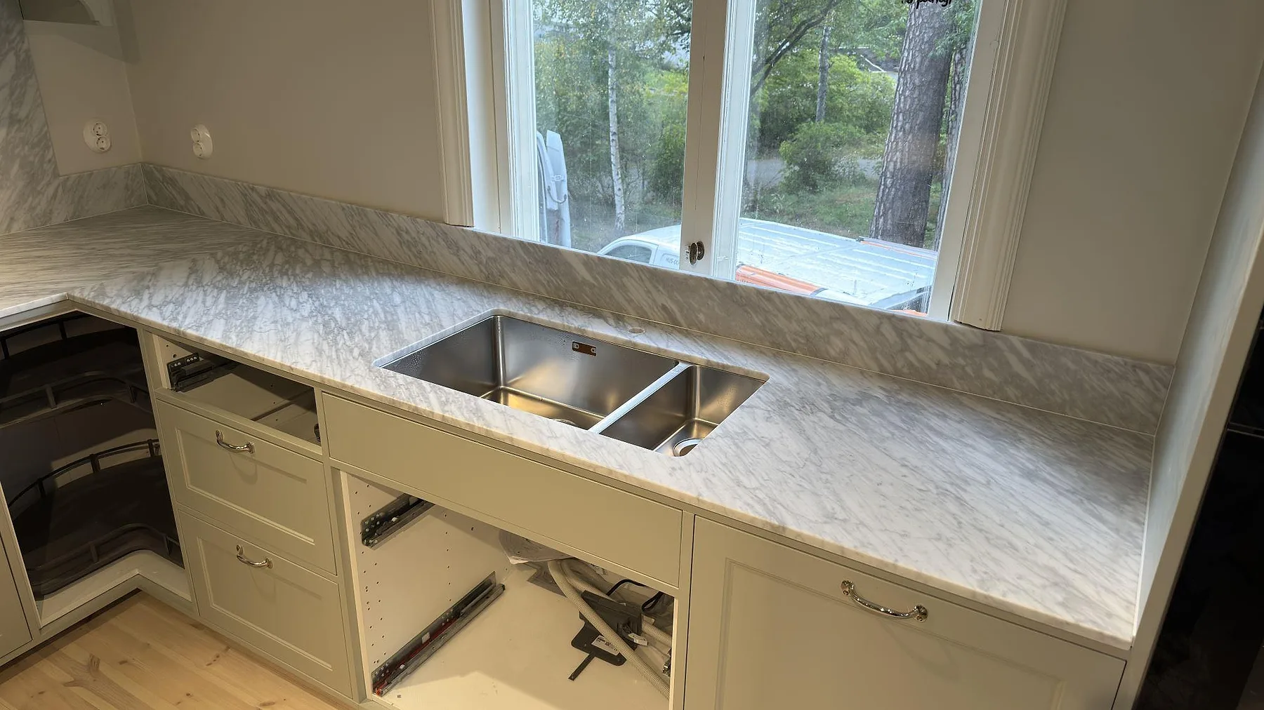 Matt Carrara C marmor vid fönstret i ett kök i Djursholm, med rostfri diskho och låg stänkkant i samma sten.
