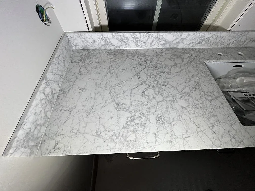 Närbild av matt Carrara C marmor som köksbänkskiva med tät grå ådring och låg stänkkant i Enebyberg.