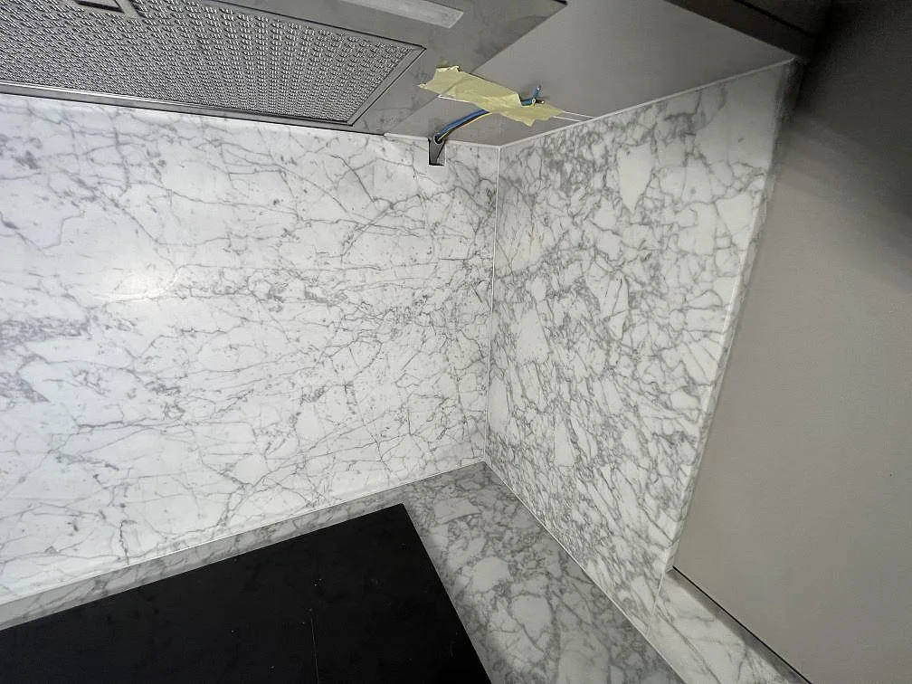 Detalj av högre stänkvägg och bänkskiva i matt Carrara C marmor vid hällen i ett kök i Enebyberg.