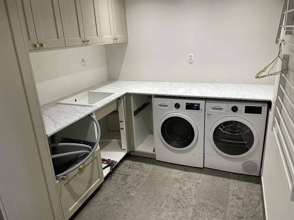 Bänkskiva i matt Carrara C marmor i en tvättstuga i Enebyberg, med underlimmad vit ho och L-formad yta över Bosch-maskiner.