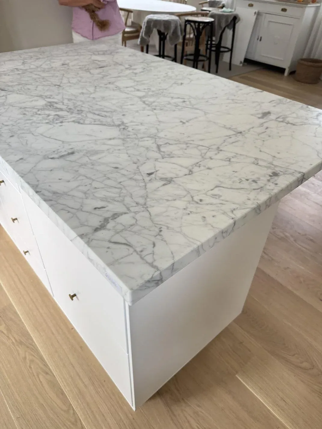 Köksbänkskiva i matt Carrara C marmor på vit köksö i Falsterbo, med tjock kant och grå ådring.