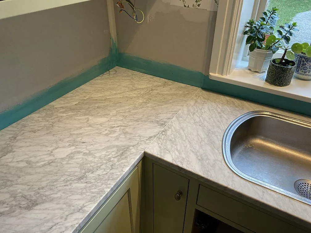 Hörndetalj i Falsterbo med matt Carrara C marmor runt diskbänksområdet, synlig ådring och väggytor under arbete.