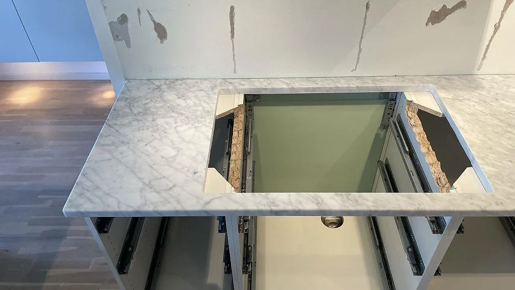 Väggbänk i matt Carrara C marmor med stort förberett urtag och öppen köksstomme i ett kök i Falsterbo.