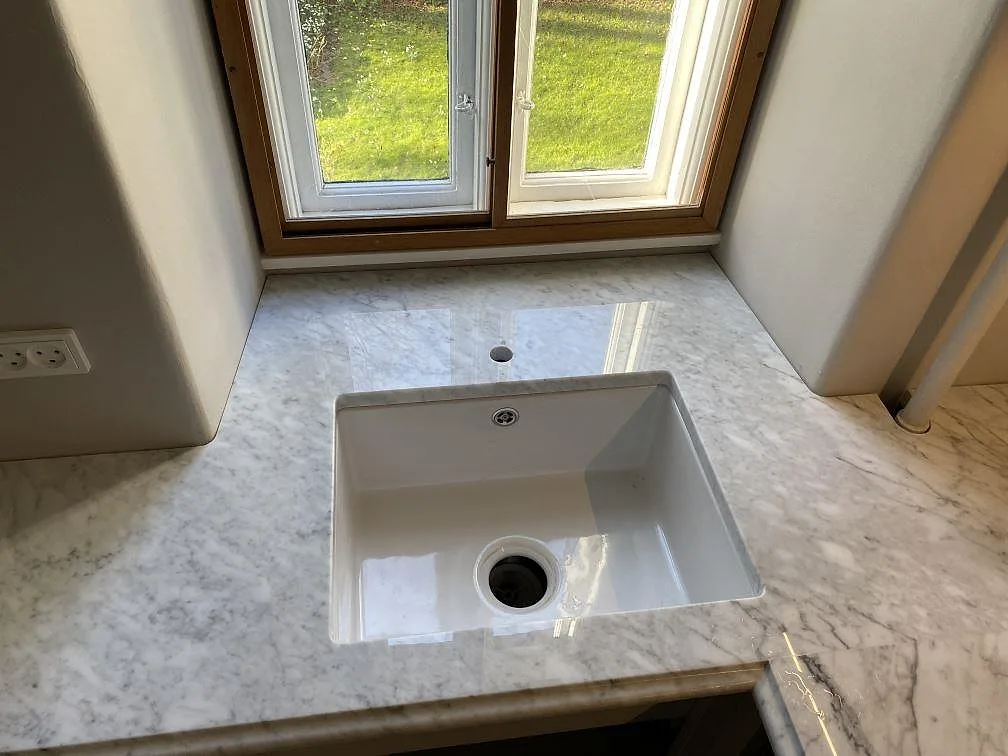 Närbild av vit diskho i polerad Carrara C-marmor vid fönster i ett kök i Frederiksberg C.