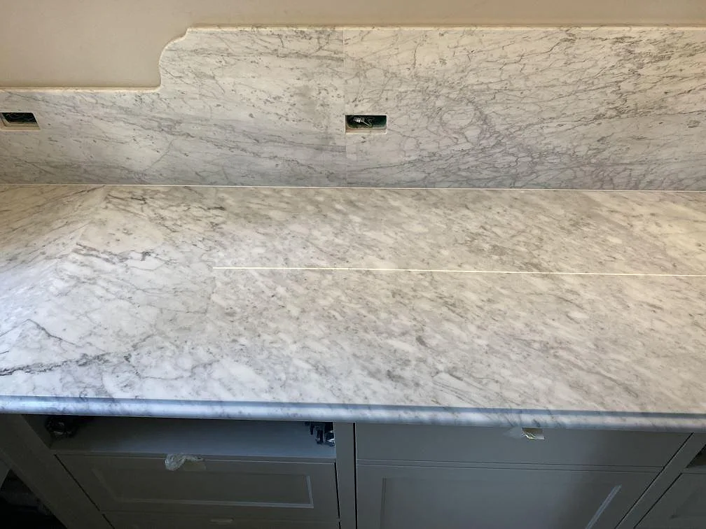 Närbild av polerad Carrara C-marmor med skarvlinje, grå ådring och uppvikt stänkkant i Frederiksberg C.