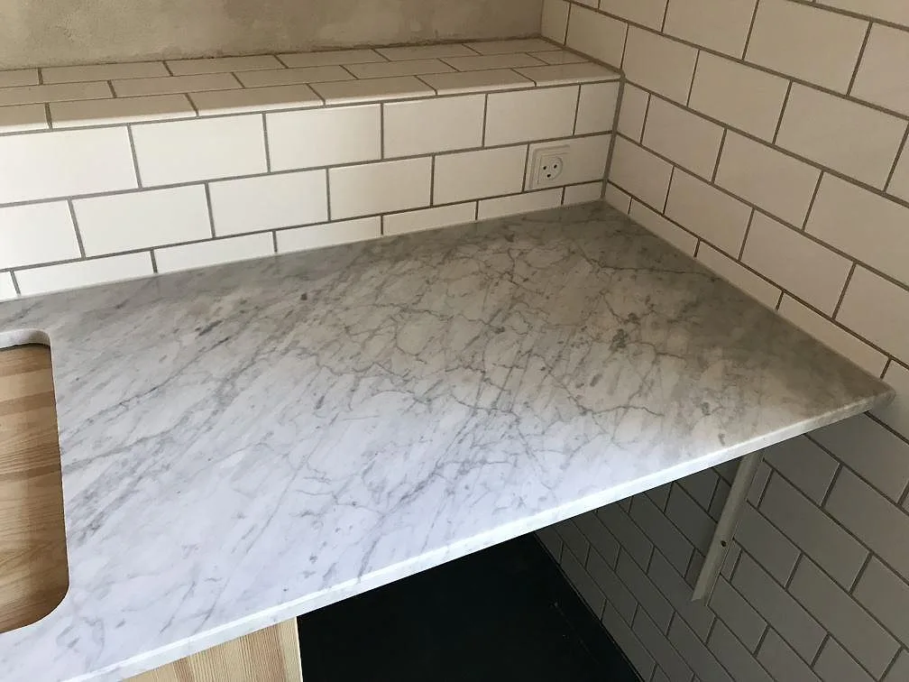 Köksbänkskiva i Carrara C marmor mot vitt kakel med urtag för diskho, matt finish, i ett kök i Gilleleje.