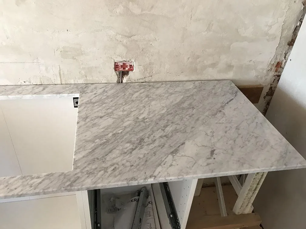 Köksbänkskiva i Carrara C marmor monterad på vita stommar med urtag för underlimmad diskho, i ett kök i Gilleleje.