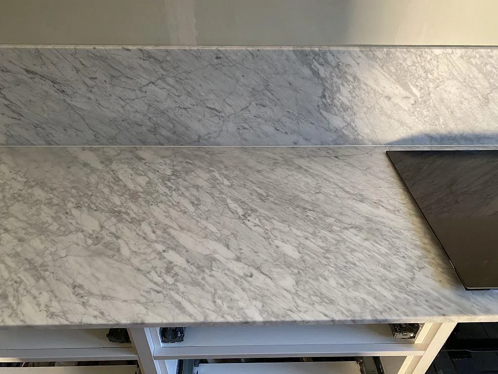 Detalj av matt Carrara C marmorbänkskiva med stänkkant och hällzon på vita köksstommar i Göteborg.