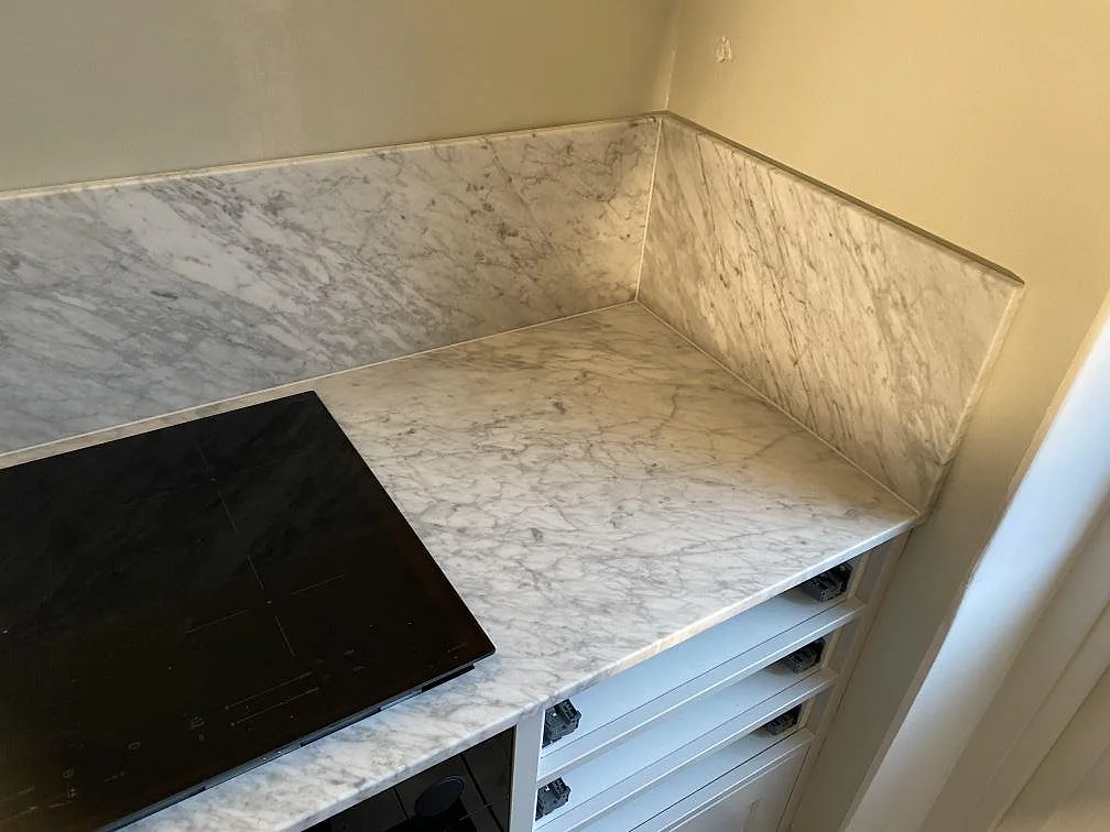 Köksbänkskiva i Carrara C marmor, matt, med uppvikt stänkskydd i samma sten och plats för induktionshäll i ett kök i Göteborg.