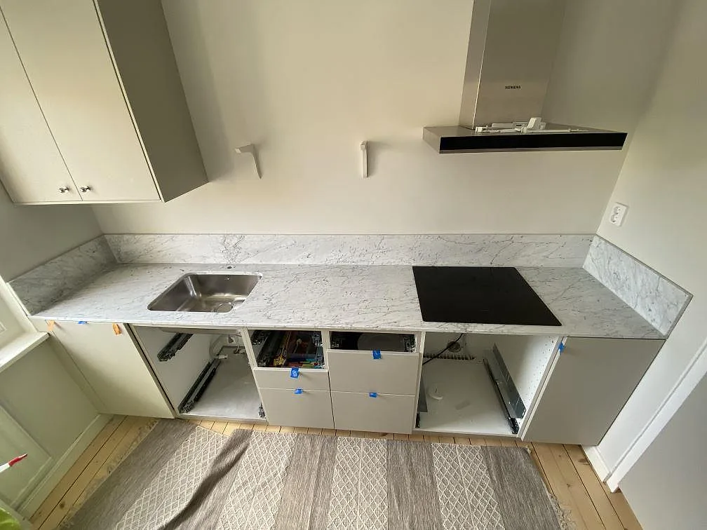 Köksbänkskiva i vit Carrara C-marmor, matt yta, med underlimmad rostfri diskho och infälld induktionshäll i ett kök under montering i Göteborg.