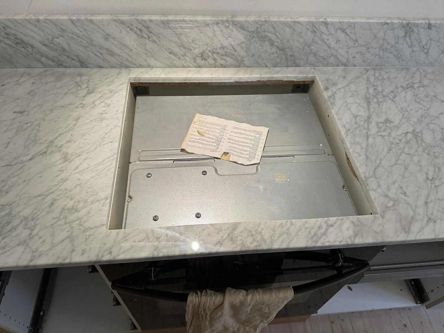 Hällurtag i polerad Carrara C marmorbänkskiva med uppvikt stänkskydd och öppna skåpstommar i ett kök i Göteborg.