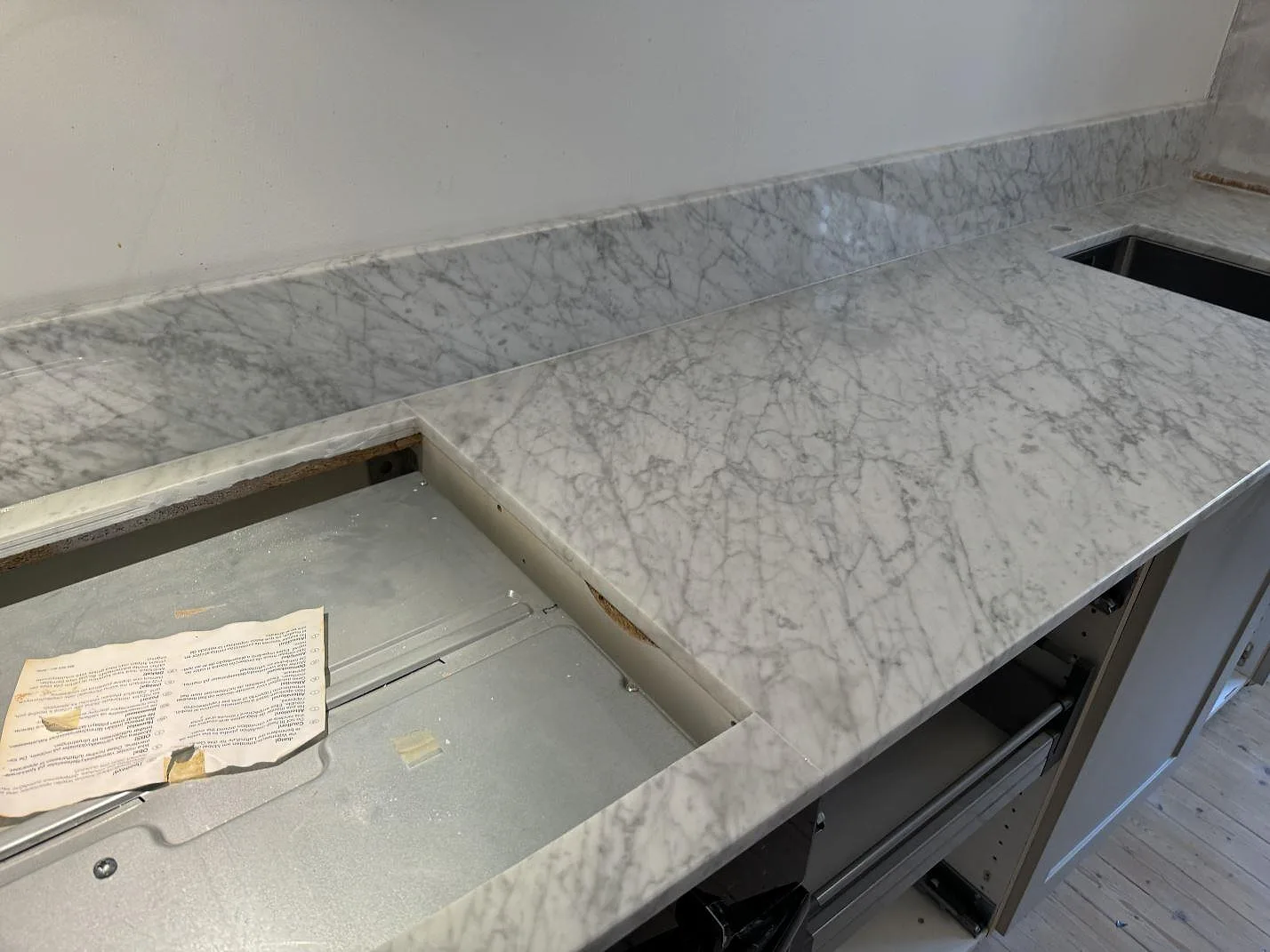 Köksbänkskiva i polerad Carrara C marmor med hällurtag, uppvikt stänkskydd och synlig L-form i Göteborg.
