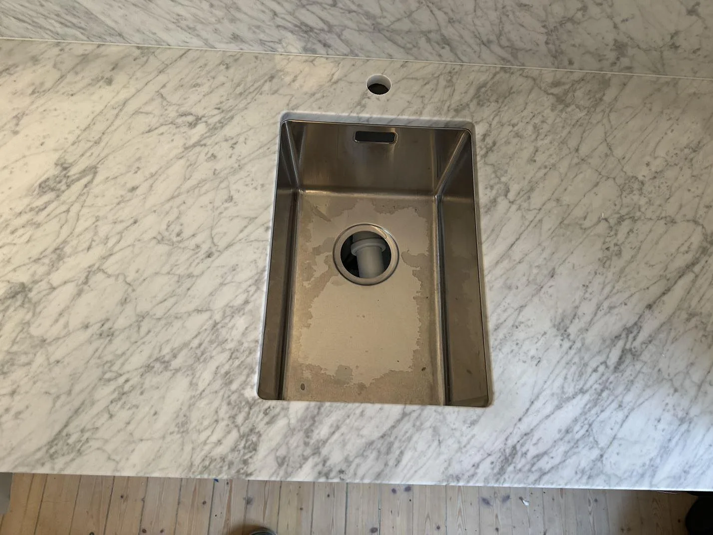 Närbild på rostfri diskho i polerad Carrara C marmor med grå ådring och blandarhål i ett kök i Göteborg.
