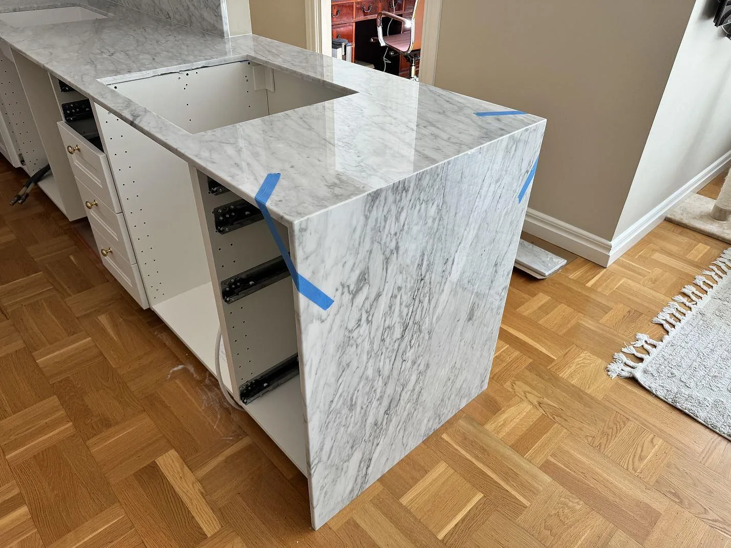 Köksö i 20 mm polerad Carrara C marmor med stenklädd sida och blå monteringstejp i ett kök i Göteborg.