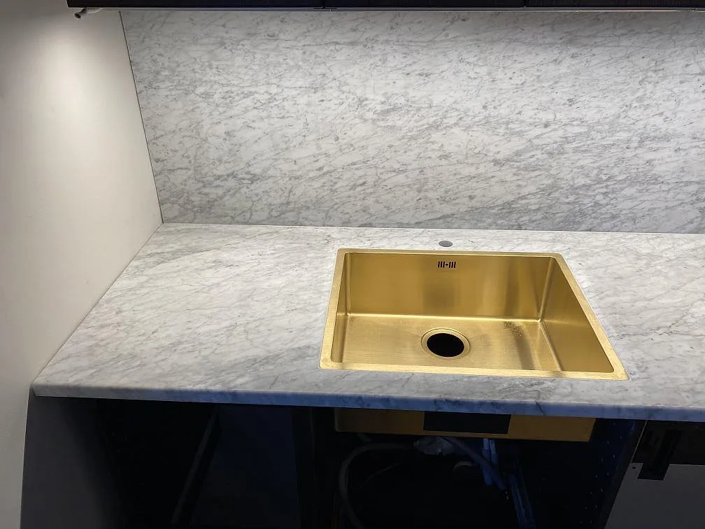 Matt Carrara C-marmor som köksbänkskiva och stänkskydd med guldfärgad diskho i ett kök i Göteborg.