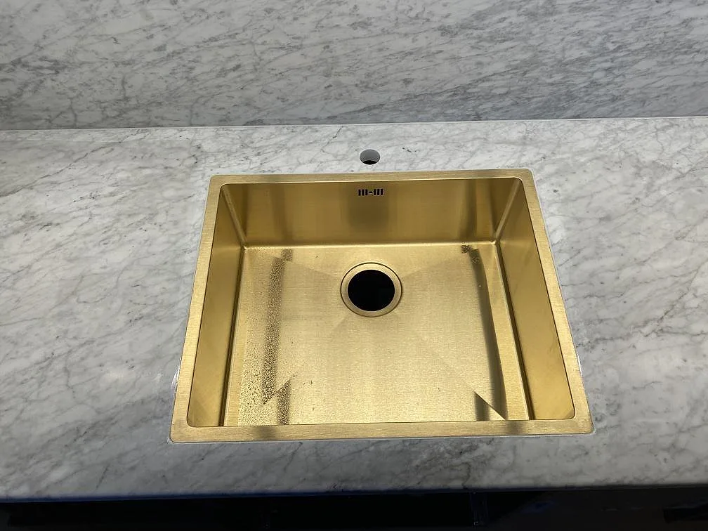 Närbild av guldfärgad diskho i matt Carrara C-marmor med grå ådring i ett kök i Göteborg.