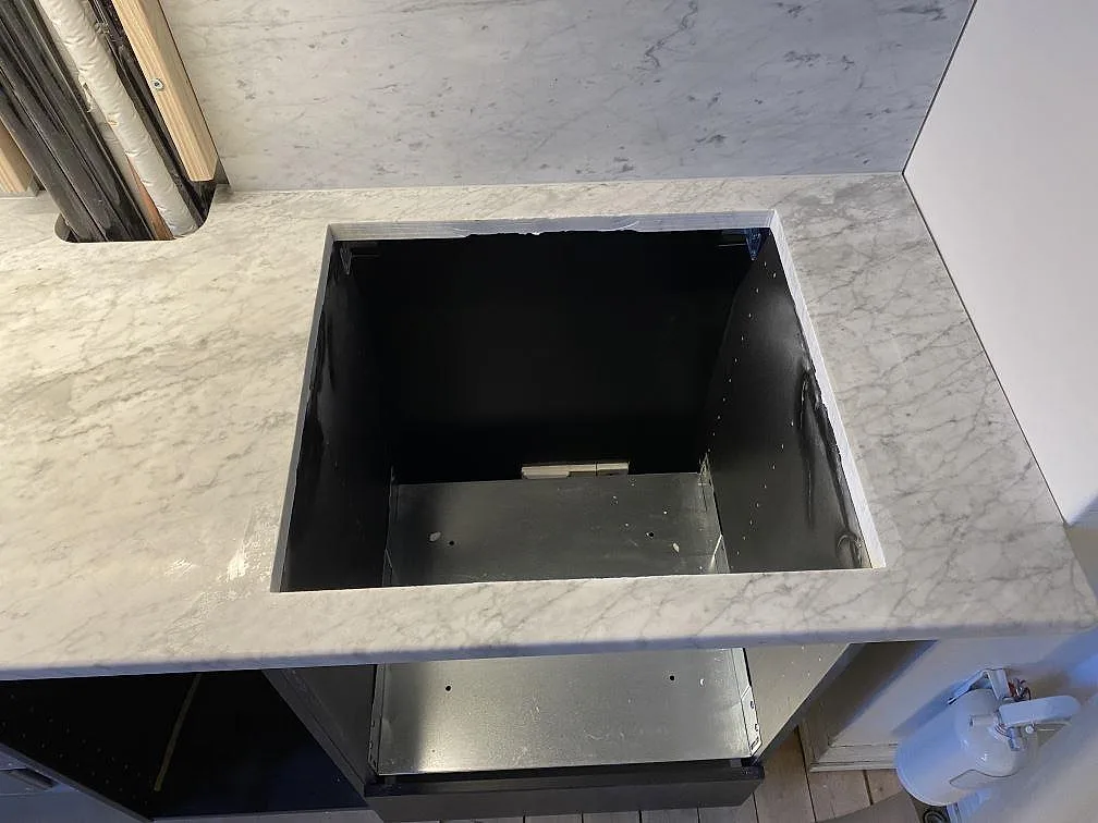 Hällöppning i matt Carrara C-marmor med stänkskydd och öppen köksstomme under montering i Göteborg.
