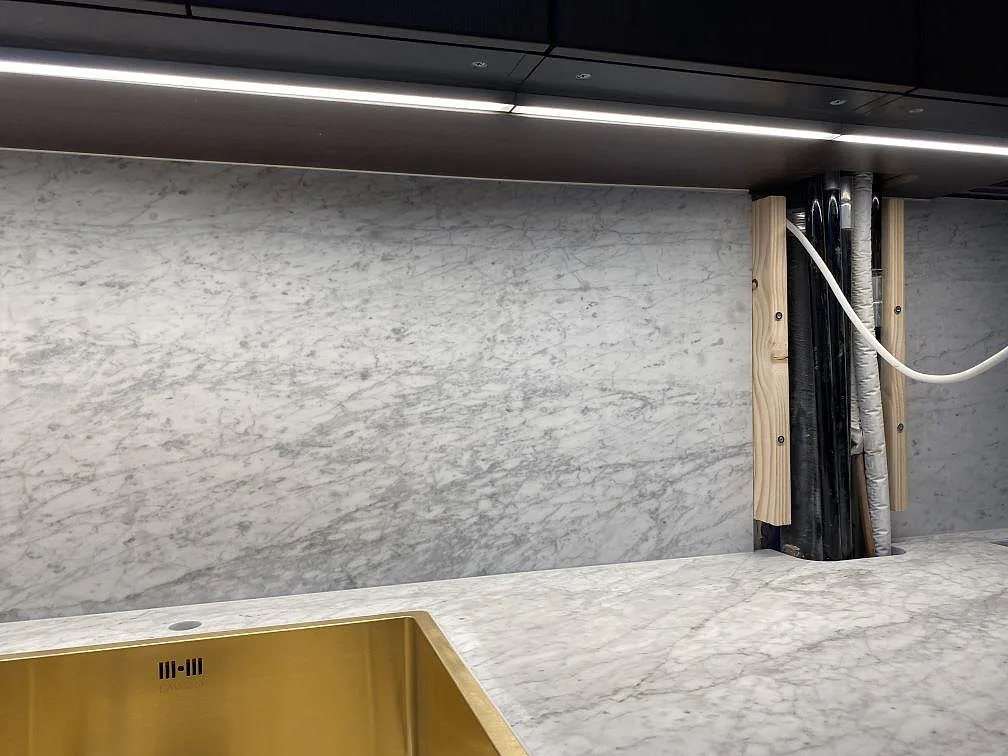 Carrara C-marmor i matt utförande som bänkskiva och stänkskydd runt synligt rörschakt i Göteborg.