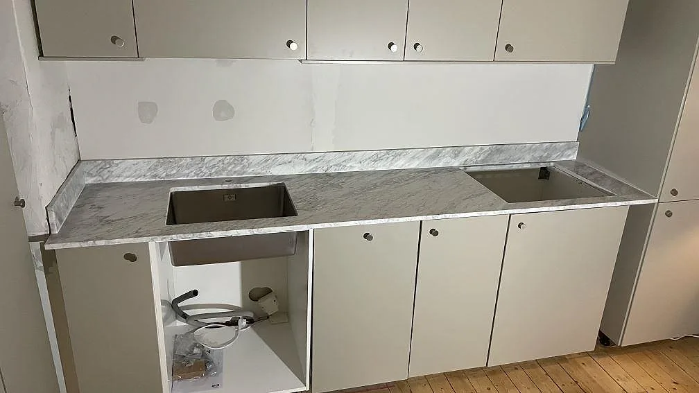 Matt köksbänkskiva i Carrara C marmor med låg stänkkant, rostfri diskho och förberedd öppning i ett kök i Göteborg.