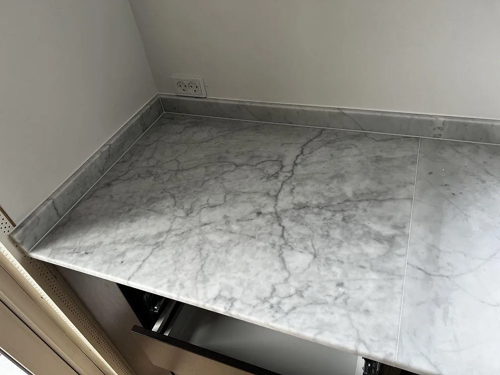Närbild av matt Carrara C marmor som köksbänkskiva med uppvikt stänkkant och tydliga grå ådror i Greve.