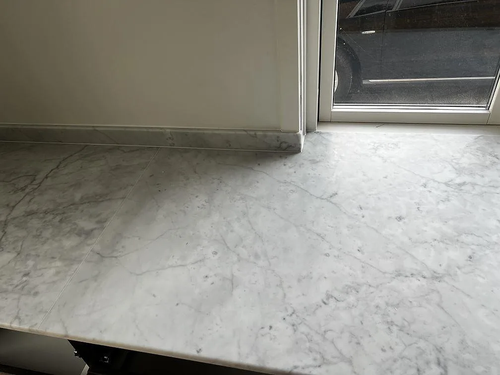 Carrara C köksbänkskiva i matt marmor vid altandörr, med låg stänkkant och ljus grå ådring i Greve.