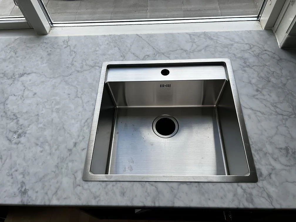 Underlimmad rostfri diskho i matt Carrara C köksbänkskiva med grå ådring och fönsterljus i Greve.