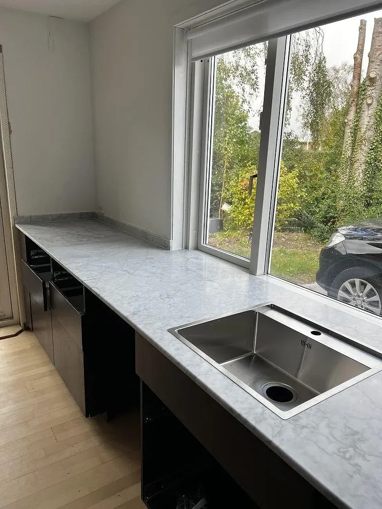 L-formad köksbänkskiva i matt Carrara C marmor, 20 mm, med underlimmad rostfri diskho vid altandörrar i Greve.
