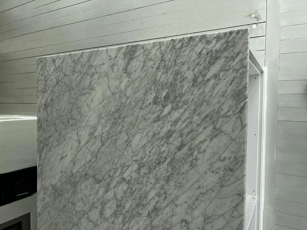 Heltäckande stenvägg i matt Carrara C marmor med grå ådring vid en vit köksinredning i Grundsund.