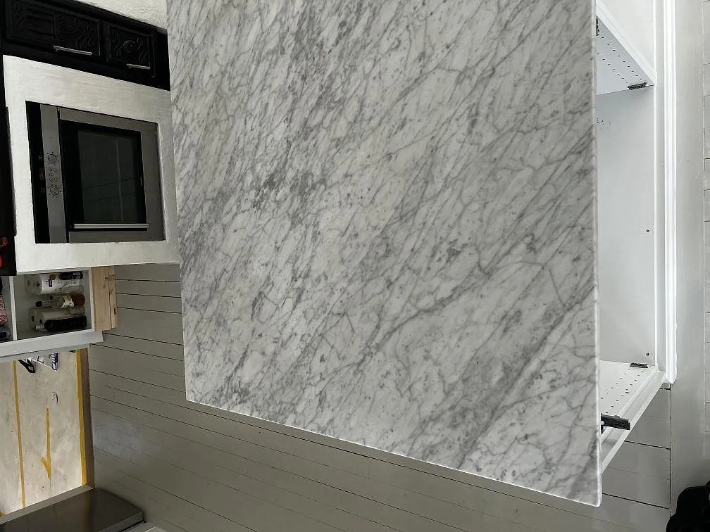 Stor väggskiva i Carrara C marmor med tydlig grå ådring och ugnsnisch i ett kök i Grundsund.