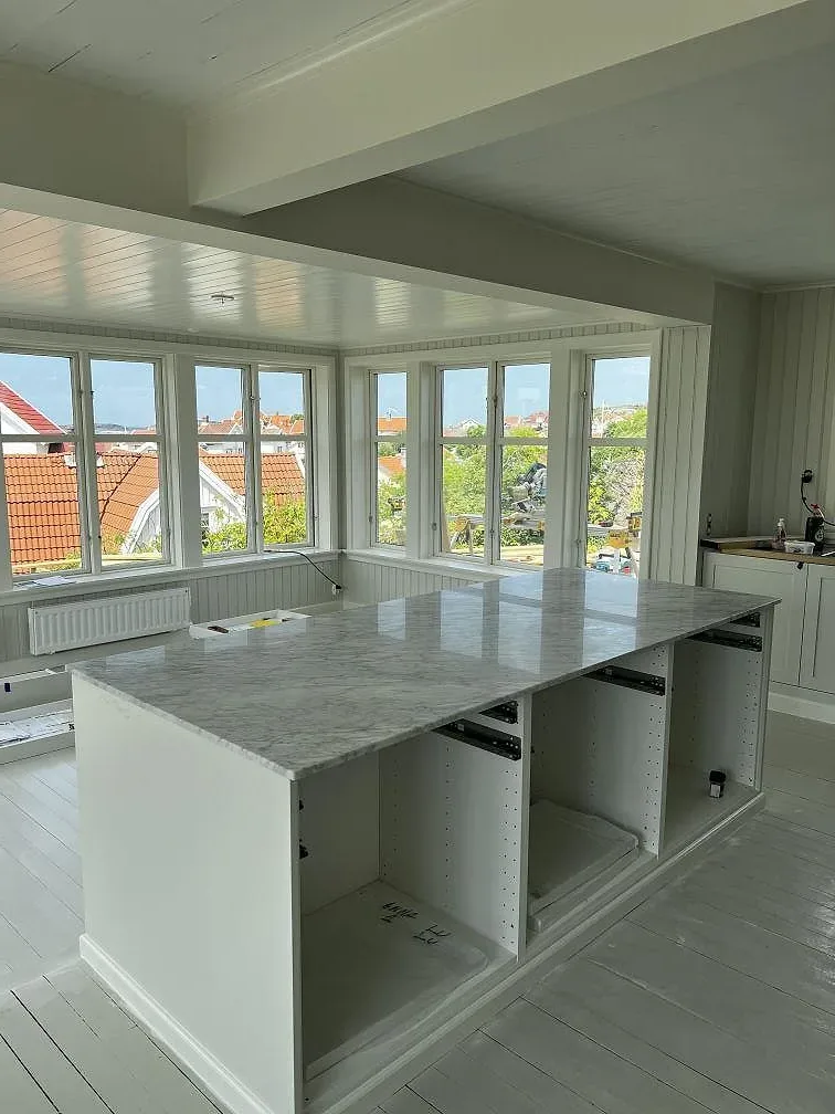 Köksbänkskiva i matt Carrara C marmor i ett vitt kök med höga fönster och takljus i Grundsund.