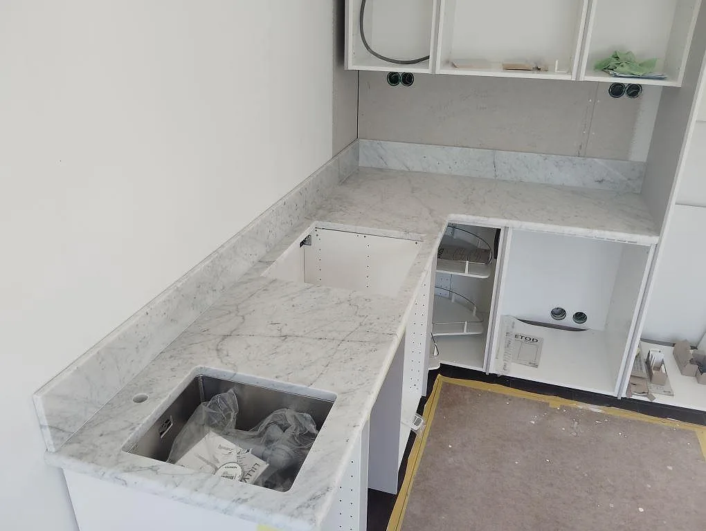 Matt köksbänkskiva i Carrara C marmor med låg stänkkant i ett L-format kök under montering i Gustavsberg.