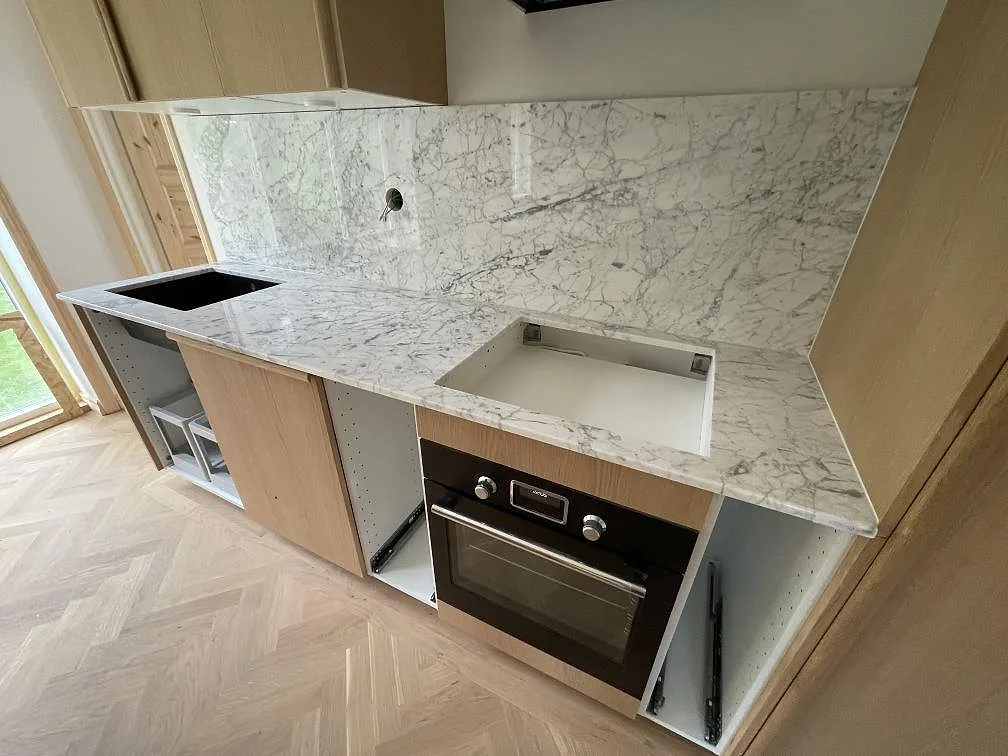 Närbild på bakre köksbänk i polerad Carrara C marmor med stänkskydd, hällöppning och diskhoöppning under montering i Hägersten.