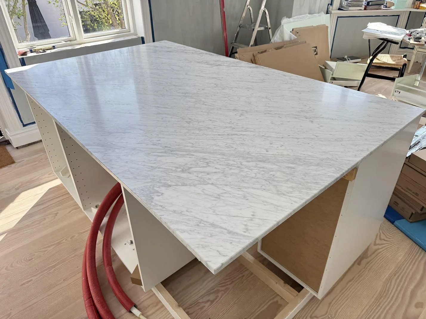 Köksö med bänkskiva i matt Carrara C-marmor, vitgrå ådring och raka kanter i ett kök i Hellerup.
