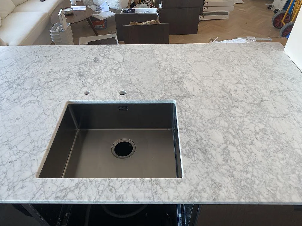 Köksbänkskiva och köksö i vit Carrara C-marmor med grå ådring, matt yta, mörka köksstommar och fiskbensparkett i ett kök i Helsingborg.